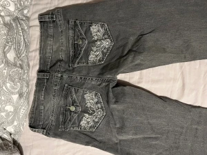 Grå jeans med broderade fickor från Gina Tricot - Snygga grå jeans från Gina Tricot med coola broderade detaljer på bakfickorna. Jeansen har normal passform och jag har sprätt upp dom längst ner för att bli något längre. Storlek M 14+