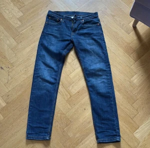 Levi's 512 blå jeans W28 L32 - Snygga blå Levi's 512 jeans med klassisk femficksdesign och smal passform. Jeansen har en mörkblå tvätt, raka ben och detaljerade sömmar. Märkeslappen i skinn sitter bak i midjan och de är tillverkade i slitstarkt bomullsjeansmaterial. Skriv vid frågor eller funderingar