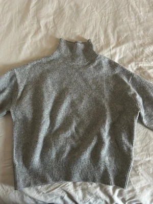 Grå polotröja från Gina Tricot - Mysig grå polotröja från Gina Tricot i storlek S. Tröjan har en hög, ribbad krage och ribbade muddar vid ärmslut och nederkant