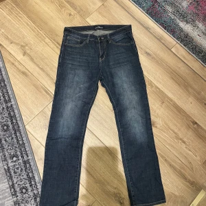 Mörkblå jeansbyxor från  - Snygga mörkblå jeansbyxor från med klassisk femficksdesign och raka ben. Jeansen har diskreta slitningar framtill och bakfickor med dekorativa sömmar. Perfekta för dig som gillar en stilren och enkel look.