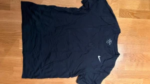 Svart Nike Dri-Fit t-shirt - Svart t-shirt från Nike med klassisk vit swoosh-logga på bröstet. Tillverkad i Dri-Fit-material som andas och håller dig torr. Enkel och stilren design med rund hals och korta ärmar, perfekt för träning eller chill.