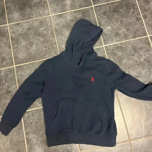 Mörkblå hoodie från Ralph Lauren - Säljer en snygg mörkblå hoodie från Ralph Lauren med det klassiska röda logotypbroderiet på bröstet. OBS liten i storleken passar mer s