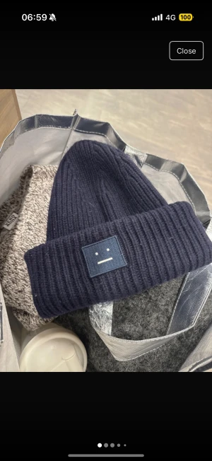 Mörkblå ribbad mössa Acne Studios - Snygg mörkblå mössa från Acne Studios med ribbad stickning och klassisk Face-logga framtill. Mössan är tillverkad i mjuk ull och har en uppvikt kant för extra stilpoäng. Perfekt för dig som vill ha en clean och trendig look under kalla dagar.