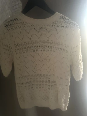Vit stickad blus med spetsmönster - Säljer en vit stickad blus med korta ärmar och vackert spetsmönster. Toppen har rund halsringning och ett luftigt, genombrutet mönster som ger en romantisk känsla. Perfekt för vår och sommar! Superfin med exempelvis Linne eller skjorta under. Bara att be om mer bilder!🥰