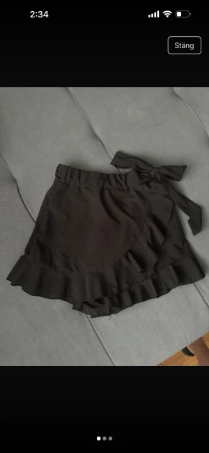 Svarta omlottshorts med volang - Snygga svarta omlottshorts med bred resår i midjan och knytband på sidan. Shortsen har volangkant längs nederdelen som ger en extra feminin touch. Perfekta för dig som gillar en trendig och lekfull stil. Materialet känns lätt och luftigt.