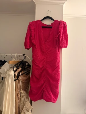 Rosa kortklänning  - Superfin rosa kortklänning från Loavies med v-ringning, puffärmar och volangdetaljer. Klänningen har broderade mönster och rynkade partier framtill som ger en snygg siluett. 