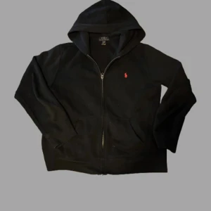 Polo Ralph Louren zip hoodie - Svart hoodie från Polo Ralph Lauren. Storlek: 14/16y sitter som xs. Skick: 9/10 bara använd fåtal gånger ingenting är sönder. Köpt för: 1100 i Spanien på corte ingles. Priset ej hugget i sten kom med bud!