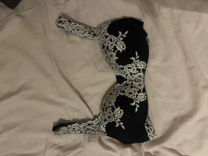 Svart bandeau tubtopp med spets - Säljer en svart bandeau tubtopp med vit spetsdetalj i blommigt mönster. Toppen är axelbandslös och har en elegant, feminin look som passar perfekt till en snygg outfit. Spetsen ger en lyxig känsla och gör toppen extra speciell.