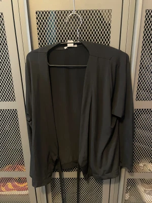 Svart omlott cardigan jacka med knyt - Svart cardigan jacka från H&M i mjukt och lätt material. Jackan har omlottmodell med knytband i midjan och långa ärmar. Enkel och stilren design som passar perfekt till lager-på-lager och chill outfits.