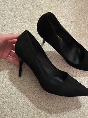 Svarta pumps från Wanzhillin - Snygga svarta pumps från Wanzhillin med spetsig tå och hög klack. Skorna är tillverkade i mocka och har en elegant, stilren design som ger en cool och sofistikerad vibe. Perfekta för dig som gillar klassiska och trendiga skor med attityd.