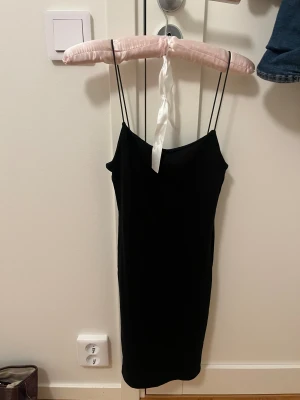 Svart miniklänning  från Zara - En svart, enkel och stilren  miniklänning från Zara med tunna axelband och rak passform. Klänningen är knälång och har en minimalistisk look som är lätt att styla med accessoarer. Perfekt för dig som gillar en clean och klassisk vibe.