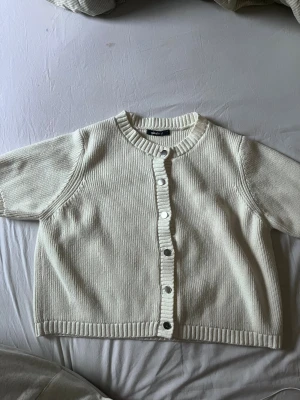Vit kortärmad kofta från Gina Tricot - Supersöt vit kofta från Gina Tricot med korta ärmar och rund hals. Den är ribbstickad med knappar framtill. Croppad passform. Kommer ej till nån användning längre. 
