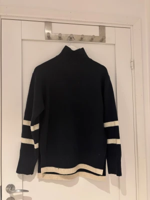 Svart polotröja med vita ränder - Snygg svart polotröja med ribbad krage och vita ränder på ärmarna samt nederkanten. Tröjan har lång ärm och en loose passform, och inte alls sticksig. Säljer bara då den inte passar mig längre