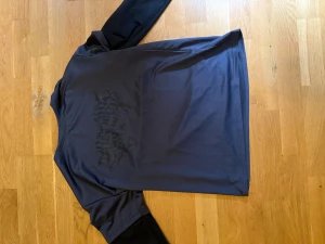 långärmad tröja med tryck - Långärmad tröja med svarta ärmar och ett diskret svart tryck på ryggen. Tröjan har en clean look och är gjord i ett mjukt syntetmaterial som känns skönt mot huden. Perfekt för dig som gillar streetwear och vill ha något unikt i garderoben.