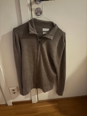 Beige merinoull kofta These Glory Days - Snygg beige kofta från These Glory Days i mjuk superior merinoull. Modellen har hel dragkedja framtill, krage och långärmad passform. Perfekt för dig som gillar stilrena och enkla plagg med lite extra premiumkänsla. Passar dig som vill ha en normal passning.