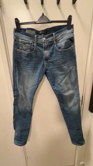 Replay blå jeans tapered fit 31/32 - Snygga blå jeans från Replay med klassisk femficksdesign och coola kontrastsömmar på bakfickorna. Modellen har tapered fit och normal passform, med medelblå tvätt och lätt slitna detaljer. Perfekt för dig som gillar stilrena och bekväma jeans. Väldigt fint skick men behövs strykas vilket görs innan leverans 