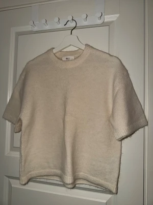 Beige stickad tröja Gina Tricot S - Mysig beige stickad tröja från Gina Tricot i ullblandning. Modellen har korta ärmar, rund hals och ribbade kanter. Perfekt för lager-på-lager och chill stil. Enkel och clean design som funkar till många looks.