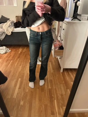 Raka jeans - Säljer ett par klassiska jeans i mörkblå tvätt med snygga kontrastsömmar. Modellen har bootcut-ben och normal passform, samt fem fickor och knappgylf. Perfekt för dig som gillar tidlös denimstil och vill ha jeans med lite vidare benslut.