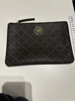 By Malene Birger Ivy Purse – Dark Chokolate - By Malene Birger Ivy Purse – Dark Chokolate Insida av bomull 25,5 x 18cm Läderklädsel  Adorned with the Signature Flower print, the Ivy purse is made to store your most important items. The Malene Birger Ivy purse is a stylish way to carry everyday essentials.    Se gärna mina andra annonser!