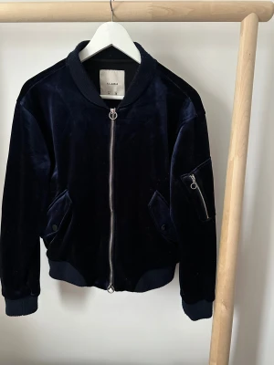 Mörkblå bomberjacka Pull&Bear - Snygg mörkblå bomberjacka från Pull&Bear i mjuk sammet. Jackan har ribbade muddar, dragkedja framtill och fickor med tryckknappar. Extra ficka med dragkedja på ärmen.