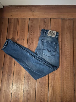 Replay Anbass jeans blå slim fit - Säljer ett par Replay Anbass jeans i klassisk blå tvätt med snygga slitningar. Modellen är slim fit med raka ben och femficksdesign. Jeansen har tydliga Replay-detaljer och är tillverkade i mjukt jeanstyg som sitter skönt hela dagen.