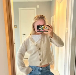 Beige kofta från Zara med knappar - Supermjuk beige kofta från Zara med v-ringning och snygga knappar framtill. Koftan är stickad och har lång ärm, perfekt att slänga över en t-shirt eller linne. Enkel och stilren modell som är lätt att matcha med jeans eller kjol.