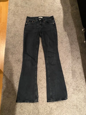Bootcut lågmidjade  jeans - Snygga svarta bootcut jeans från Gina i storlek 34. Klassisk femficksmodell med dragkedja och knapp framtill. Jeansen har en mörk tvätt och är tillverkade i mjukt denim-material som sitter skönt. Perfekt för dig som vill ha något som passar till allt🩷🩷