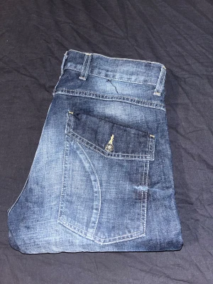 Blå jeans från Grant - Snygga blå jeans från Grant med slitna detaljer och kontrastsömmar. Modellen har raka ben, klassiska fem fickor och coola knappar på bakfickorna. Jeansen är tillverkade i robust denim och har en modern tvättad look.
