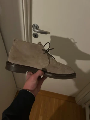 Beige mockakängor Brunello Cucinelli - Snygga beige kängor från Brunello Cucinelli i mjuk mocka med rund tå och platt sula. Skorna har klassisk snörning och stilren design som passar till många outfits. Tillverkade i Italien med exklusiv känsla och detaljerad söm längs sulan.