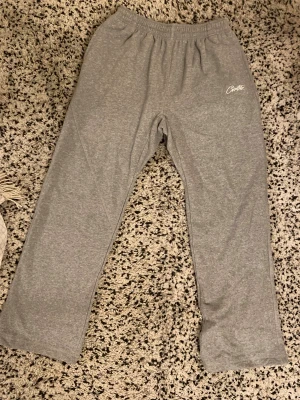 Grå mjukisbyxor från Corteiz XL - Säljer ett par grå mjukisbyxor från Corteiz i storlek XL. Byxorna har elastisk midja, fickor och vit broderad logga på framsidan. Materialet är mjukt och skönt, perfekt för chill dagar. Snyggt streetwear-plagg med enkel design och bekväm passform.