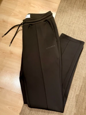 Bruna mjukisbyxor från Les Deux - Bruna mjukisbyxor från Les Deux med stilren design och diskret logga på benet. Byxorna har ribbad midja med snörning och raka ben. Perfekta för chill eller streetwear, tillverkade i mjukt material för extra komfort. Pris i affär 1199kr. Passar både S och M, herrstorlek! 