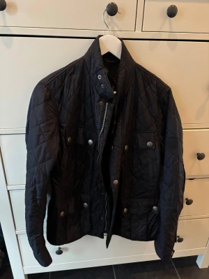 Svart quiltad Barbour jacka S - Väldigt fint skick nästan aldrig använd Perfekt höstjacka  Nypris 3200 kr, Quiltad svart jacka från Barbour i storlek S. Jackan har snygga tryckknappar med Barbour-logga, ståkrage och flera fickor framtill. Insidan har coolt motorcykeltryck. Perfekt för dig som gillar klassisk stil med edge.