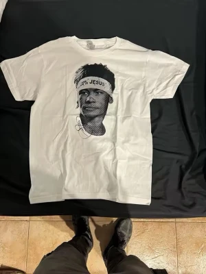 Vit Off-White t-shirt med Neymar Jr tryck - Vit t-shirt från Off-White med svart grafiskt tryck av Neymar JR på framsidan och stor sköld med pilar och stjärnor på baksidan. Klassisk passform och rund halsringning. Perfekt för dig som gillar streetwear och unika prints.