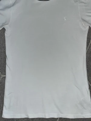 Vit t-shirt från Ralph Lauren - Klassisk vit t-shirt från Ralph Lauren med diskret broderad logga på bröstet. T-shirten har korta ärmar och rund halsringning. Tillverkad i mjuk bomull för en skön och enkel stil som funkar till allt. (Äkta)