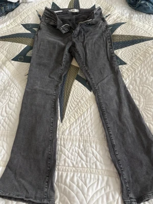 Grå bootcut jeans i bomull - Snygga grå bootcut jeans med klassisk femficksdesign och normal passform. Jeansen har en lätt utsvängd benslut och är tillverkade i mjukt bomullsmaterial. Perfekta för dig som gillar en avslappnad men trendig look. Lite slitna längst ner, se bilder. Har satt fast ett snöre så att de sitter bättre. 