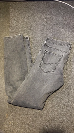 Grå slim fit jeans SLM/GLENN - Snygga grå jeans från SLM/GLENN i slim fit-modell. Klassisk femficksdesign och raka ben. Jeansen är tillverkade i mjukt denimtyg och har en stilren look som passar till det mesta.