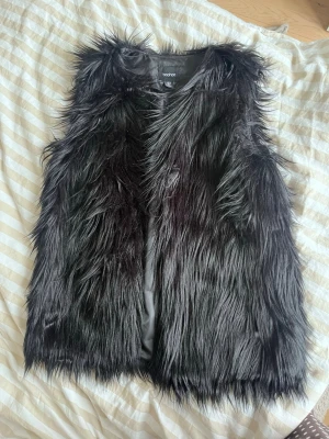Svart långhårig pälsväst från Boohoo - Säljer en svart långhårig pälsväst från Boohoo. Västen har en cool, fluffig look med fuskpäls och är helfodrad på insidan. Perfekt för att lyfta vilken outfit som helst med extra edge.
