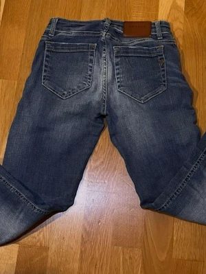 Mörkblå jeans från Dondup - Snygga mörkblå jeans från Dondup med klassisk femficksdesign och raka ben. Jeansen har en läderpatch med logga bak i midjan och subtila slitningar för en cool look. Perfekta till vardags och passar till det mesta.