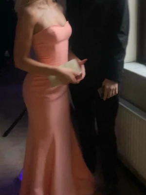 Lång rosa axelbandslös klänning - Säljer en elegant långklänning i en mjuk rosa nyans. Klänningen är axelbandslös med figurnära passform upptill och utsvängd kjol nertill. Perfekt för bal eller festliga tillfällen. 