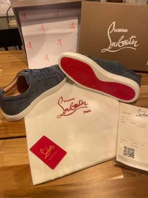 Blå mocka sneakers från Louboutin - Snygga blå sneakers från Christian Louboutin i mjuk mocka med klassisk röd sula och vita kanter. Skorna har rund tå, snörning och diskreta sömdetaljer. Perfekta för dig som vill ha en exklusiv och stilren look. Helt nya aldrig använda 10/10 skick. Skriv vid minsta fundering!