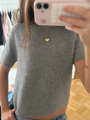 Grå stickad topp från Zara - Mysig grå stickad topp från Zara med korta ärmar och rund halsringning. Toppen har en enkel, clean look och är gjord i ett mjukt material som känns skönt mot huden. Perfekt att styla med jeans eller kjol för en chill vibe.