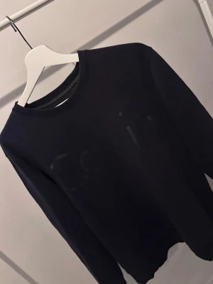 Mörkblå sweatshirt från Calvin Klein - Snygg mörkblå sweatshirt från Calvin Klein med diskret logga framtill. Tröjan har rund halsringning och ribbade muddar vid ärmslut och nederkant. Perfekt för en clean och stilren look.