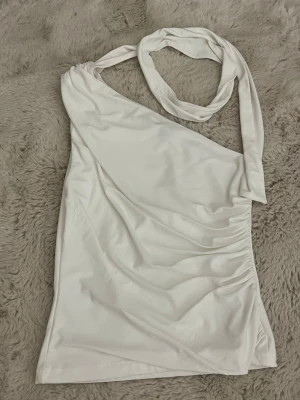 Vit oneshoulder topp Gina Tricot - Säljer en vit oneshoulder topp från Gina Tricot i storlek XS. Toppen har en asymmetrisk axel med bred axelrem och är tillverkad i mjukt, stretchigt material. Perfekt för dig som vill ha en trendig och stilren look.