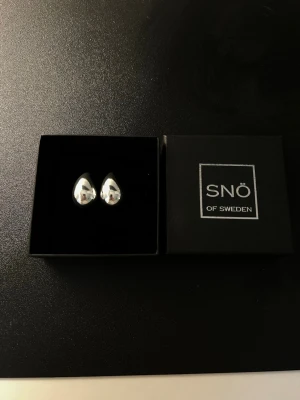 Silvriga droppformade örhängen SNÖ - Säljer ett par stilrena droppformade örhängen från SNÖ of Sweden. Örhängena är i blankt silverfärgat metallmaterial och har klassisk pluppstängning. 