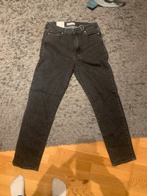 Mörkgrå  jeans med hög midja - Snygga mörkgrå mom fit jeans med hög midja och klassisk femficksdesign. Jeansen har smal passform och raka ben, perfekta till en avslappnad streetstyle-look. Tillverkade i mjukt denimtyg för skön känsla hela dagen. Säljer på grund av att de inte riktigt var min stil! Därav priset!😅🫶🏽