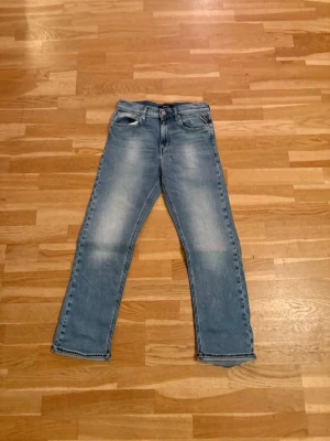 Replay Modell thad ljusblå raka jeans - Klassiska Replay jeans i ljusblå tvätt med raka ben och femficksmodell. Jeansen har knappgylf och subtila slitningar framtill för en avslappnad look. Perfekta för dig som gillar tidlös stil och vill ha ett par ikoniska jeans i garderoben.