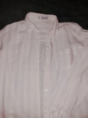 Vit randig linne skjorta från MNG Basics - Klassisk vit skjorta från MNG Basics med diskreta vertikala ränder och bröstficka. Skjortan har långa ärmar och knäppning framtill. Tillverkad i ett lätt och luftigt material som känns skönt mot huden.