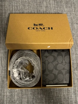 Coach - Bälte och Plånbok - Coach-box med både bälte och plånbok. Plånboken är sparsamt använd och bältet är i nyskick. Båda har samma mönster. Ej äkta läder.