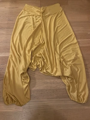 Gula loose leggings med dragsko - Snygga gula leggings med lös passform och dragsko i midjan. Tillverkade i ett mjukt och glansigt syntetmaterial som ger en cool och avslappnad vibe. Perfekta för dig som gillar unika och bekväma plagg med extra mycket rörelsefrihet.