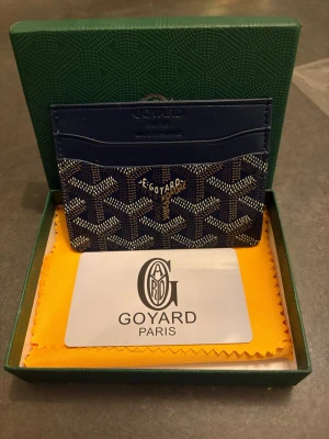 Blå G korthållare i skinn - Snygg blå korthållare från G med ikoniskt mönster i vitt och mörkblå färg.Tillverkad i exklusivt skinn och har flera fack för kort. Perfekt accessoar för dig som vill ha något både stilrent och lyxigt i fickan.